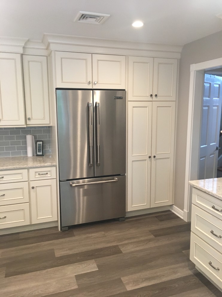 This is an example of a large traditional u-shaped kitchen/diner in New York with a submerged sink, recessed-panel cabinets, white cabinets, engineered stone countertops, blue splashback, glass tiled splashback, stainless steel appliances, porcelain flooring, grey floors and white worktops.