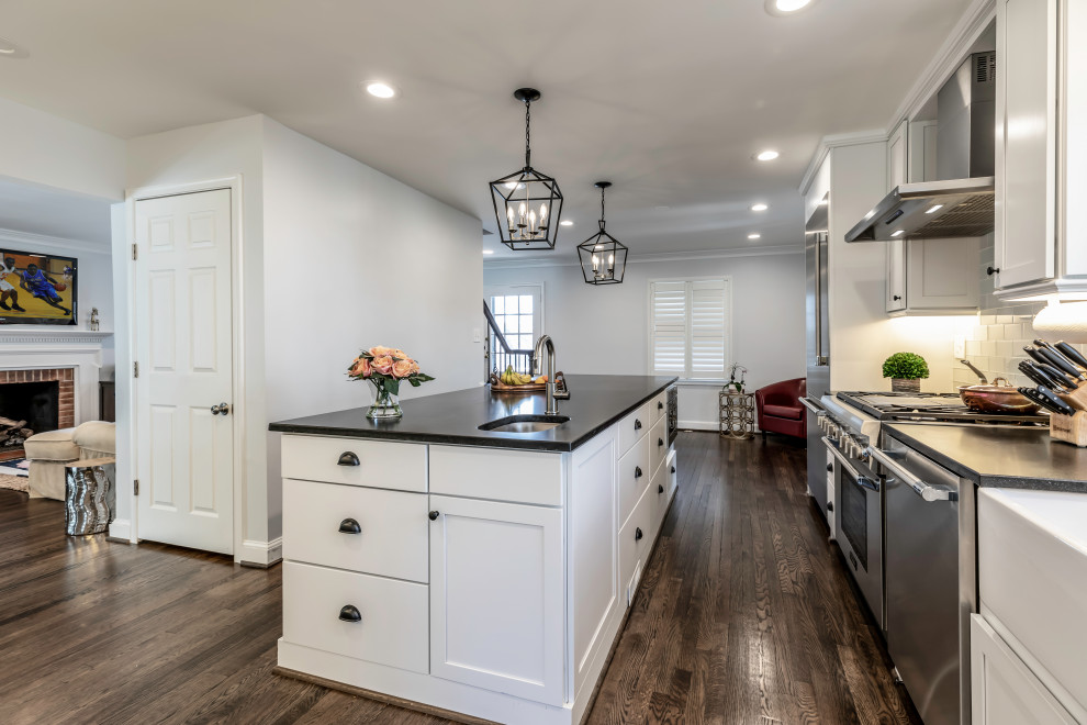 Contemporary kitchen in DC Metro with white cabinets, composite countertops, grey splashback, stainless steel appliances, medium hardwood flooring, an island, brown floors and black worktops.