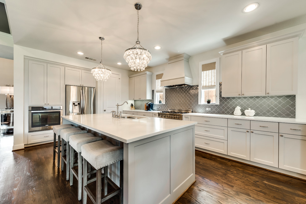 Design ideas for a large traditional l-shaped open plan kitchen in Dallas with a double-bowl sink, shaker cabinets, grey cabinets, grey splashback, porcelain splashback, stainless steel appliances, dark hardwood flooring, an island, brown floors and composite countertops.
