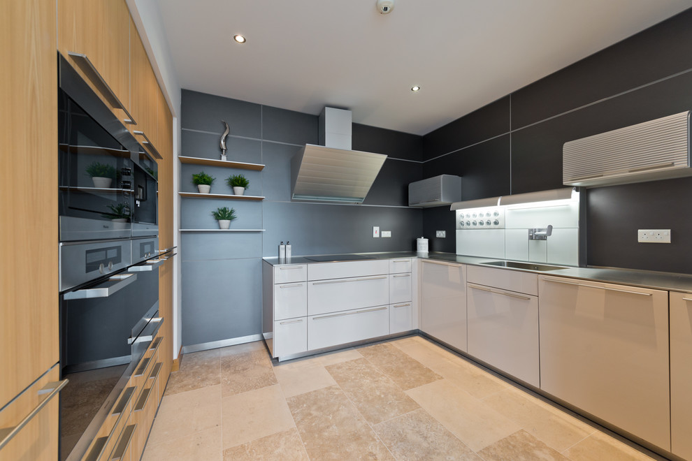 This is an example of a medium sized contemporary l-shaped enclosed kitchen in Dublin with flat-panel cabinets, black splashback, no island, beige floors, white cabinets, stainless steel worktops, black appliances and travertine flooring.
