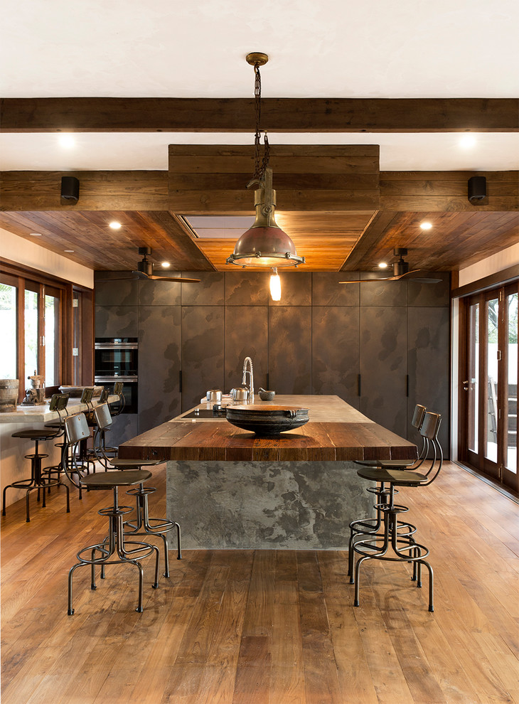 Island style medium tone wood floor and brown floor kitchen photo in Cairns with flat-panel cabinets, gray cabinets, black appliances and an island