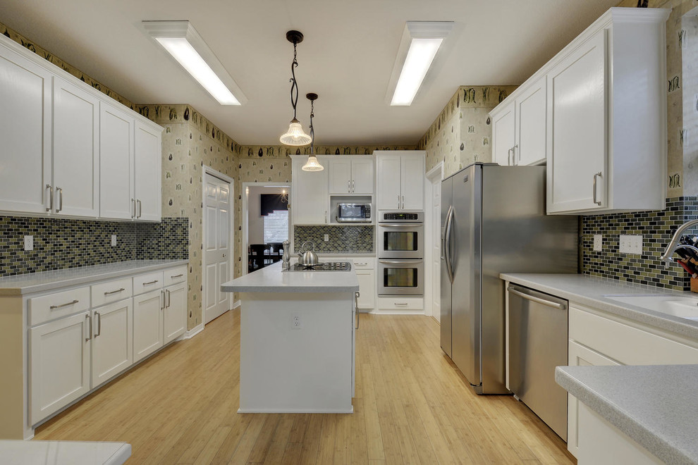 Exempel på ett klassiskt kök, med en undermonterad diskho, skåp i shakerstil, vita skåp, flerfärgad stänkskydd, stänkskydd i stickkakel, rostfria vitvaror, bambugolv, en köksö och brunt golv