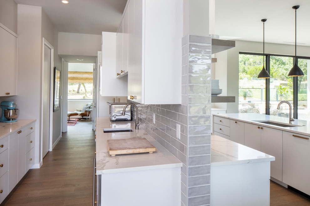 Exempel på ett stort modernt vit vitt kök, med en undermonterad diskho, släta luckor, vita skåp, marmorbänkskiva, vitt stänkskydd, stänkskydd i tunnelbanekakel, rostfria vitvaror, mellanmörkt trägolv, en köksö och brunt golv