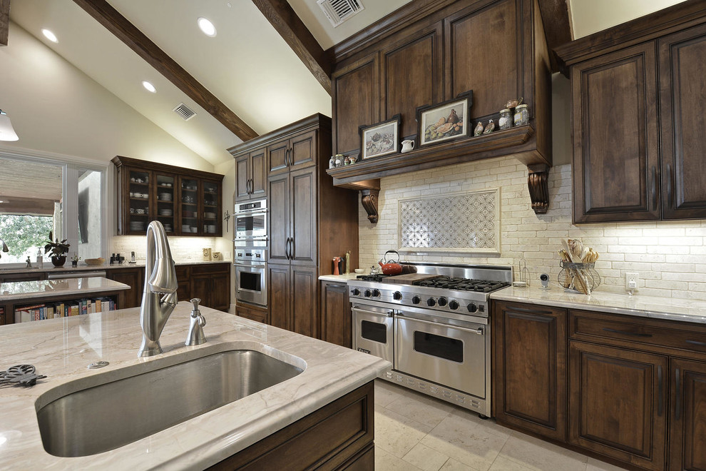 Example of a large classic l-shaped travertine floor open concept kitchen design in Austin with an undermount sink, glass-front cabinets, dark wood cabinets, quartzite countertops, beige backsplash, subway tile backsplash, stainless steel appliances and two islands
