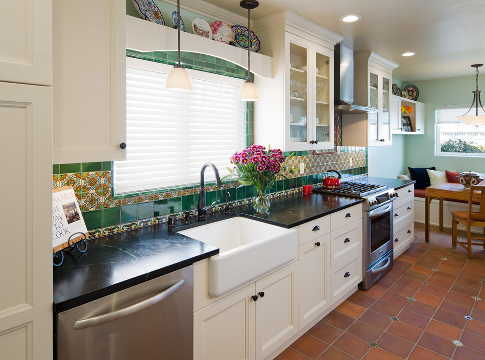This is an example of a medium sized traditional single-wall kitchen/diner in San Diego with a belfast sink, recessed-panel cabinets, white cabinets, soapstone worktops, green splashback, ceramic splashback, stainless steel appliances and terracotta flooring.