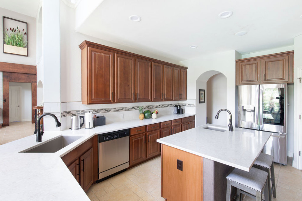 Design ideas for a classic kitchen in Austin with raised-panel cabinets, medium wood cabinets, engineered stone countertops, white splashback, ceramic splashback, stainless steel appliances, ceramic flooring, an island, beige floors and white worktops.