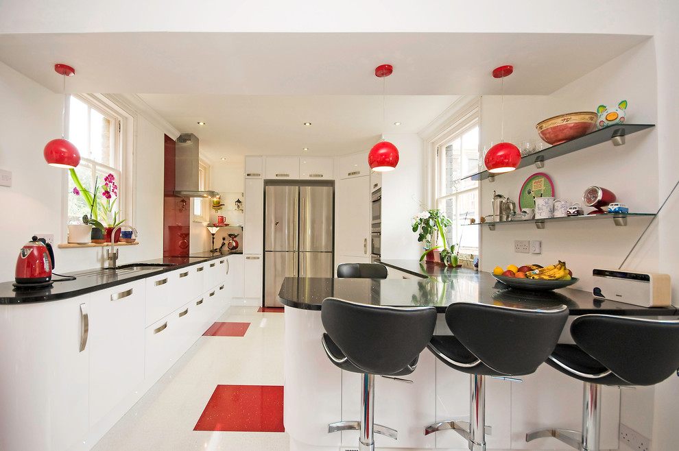 Inredning av ett modernt kök, med en undermonterad diskho, släta luckor, vita skåp, bänkskiva i kvartsit, rött stänkskydd, glaspanel som stänkskydd och rostfria vitvaror