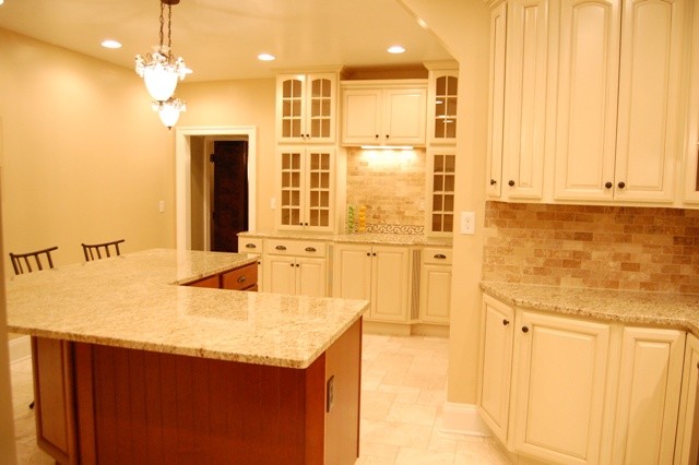Klassisk inredning av ett avskilt, stort kök, med en undermonterad diskho, luckor med upphöjd panel, vita skåp, granitbänkskiva, beige stänkskydd, stänkskydd i stenkakel, rostfria vitvaror, kalkstensgolv och en köksö
