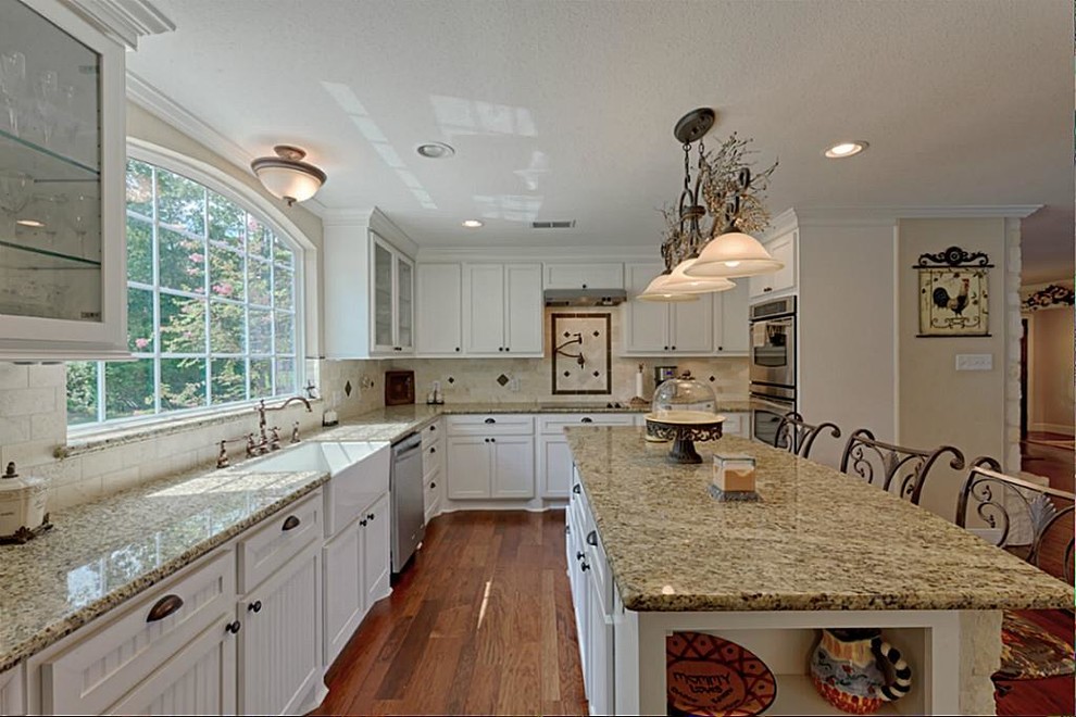 Inspiration for a large timeless l-shaped medium tone wood floor eat-in kitchen remodel in Houston with shaker cabinets, white cabinets, stainless steel appliances, an island, a farmhouse sink, granite countertops, beige backsplash and ceramic backsplash