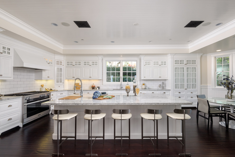 Modern inredning av ett stort grå grått kök, med en undermonterad diskho, luckor med upphöjd panel, vita skåp, vitt stänkskydd, stänkskydd i tunnelbanekakel, rostfria vitvaror, mörkt trägolv, en köksö och brunt golv