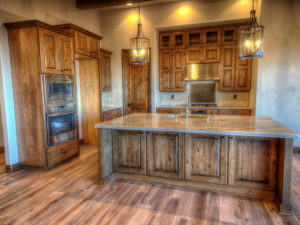 Mid-sized mountain style l-shaped medium tone wood floor eat-in kitchen photo in Other with an undermount sink, raised-panel cabinets, medium tone wood cabinets, granite countertops, beige backsplash, stone tile backsplash, stainless steel appliances and an island