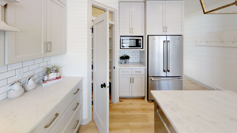 Foto de cocina comedor de estilo de casa de campo grande con puertas de armario grises, encimera de cuarzo compacto, salpicadero blanco, electrodomésticos de acero inoxidable, una isla y encimeras grises