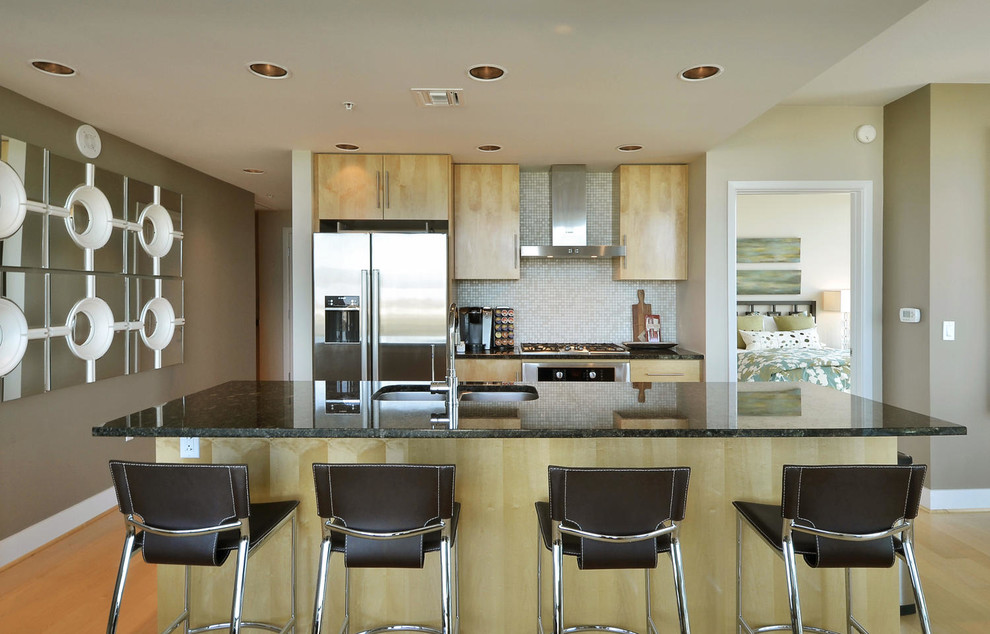 Inspiration for a small traditional galley open plan kitchen in Austin with a double-bowl sink, flat-panel cabinets, light wood cabinets, granite worktops, beige splashback, mosaic tiled splashback, stainless steel appliances, light hardwood flooring and an island.