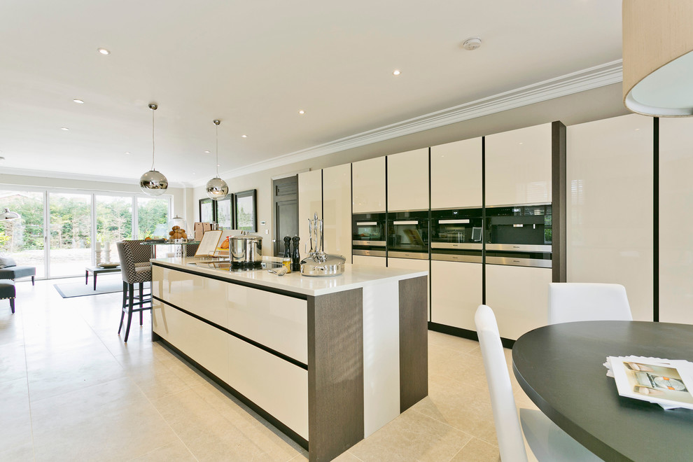 Example of a huge trendy galley open concept kitchen design in Berkshire with an undermount sink, flat-panel cabinets, beige cabinets, solid surface countertops, metallic backsplash, mirror backsplash, stainless steel appliances and an island