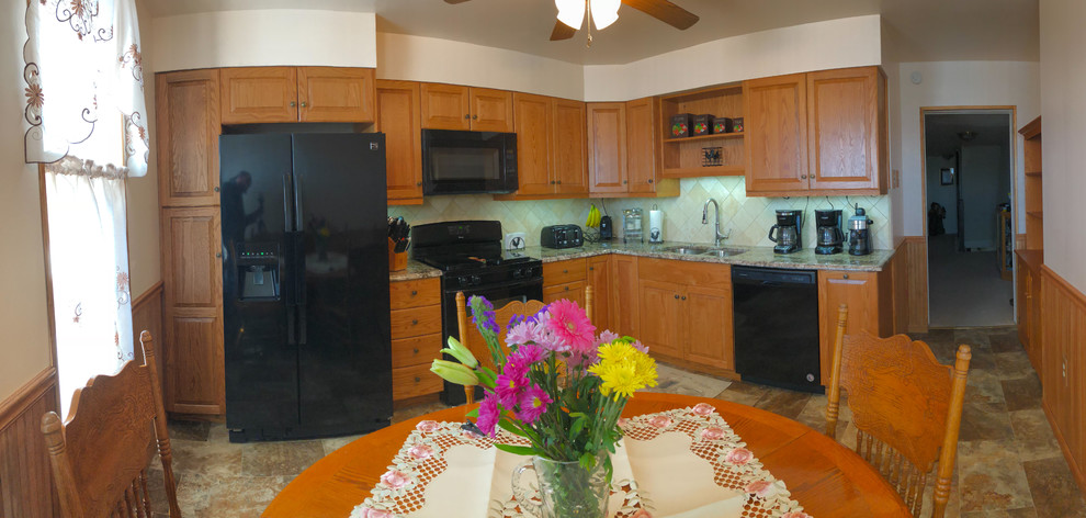 Esempio di una cucina tradizionale di medie dimensioni con lavello sottopiano, ante con bugna sagomata, ante in legno scuro, top in granito, paraspruzzi beige, paraspruzzi in travertino e elettrodomestici neri