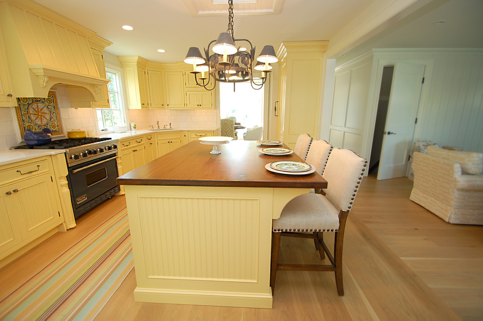 Photo of a large classic l-shaped kitchen/diner in New York with a submerged sink, beaded cabinets, yellow cabinets, engineered stone countertops, white splashback, stone tiled splashback, integrated appliances, light hardwood flooring and an island.