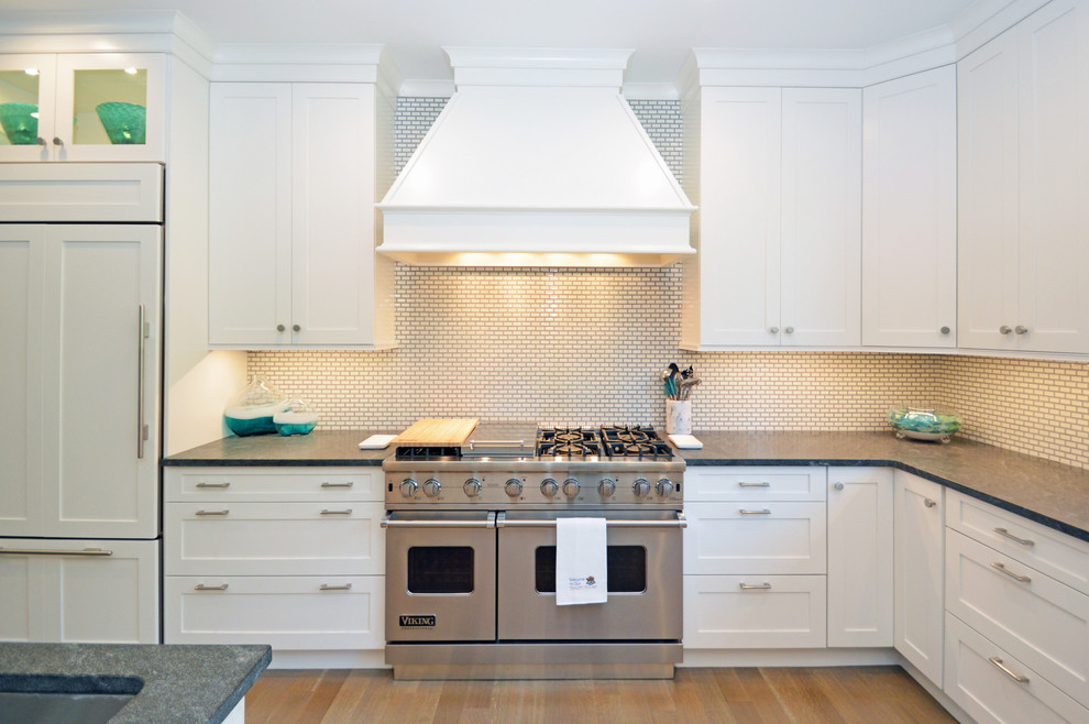 Inredning av ett klassiskt kök, med en undermonterad diskho, luckor med infälld panel, vita skåp, granitbänkskiva, vitt stänkskydd, stänkskydd i tunnelbanekakel, integrerade vitvaror, ljust trägolv och en köksö