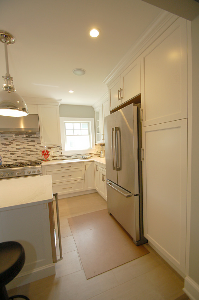 Klassisk inredning av ett litet kök, med en undermonterad diskho, luckor med infälld panel, vita skåp, bänkskiva i kvarts, grått stänkskydd, stänkskydd i mosaik, rostfria vitvaror, ljust trägolv och en köksö