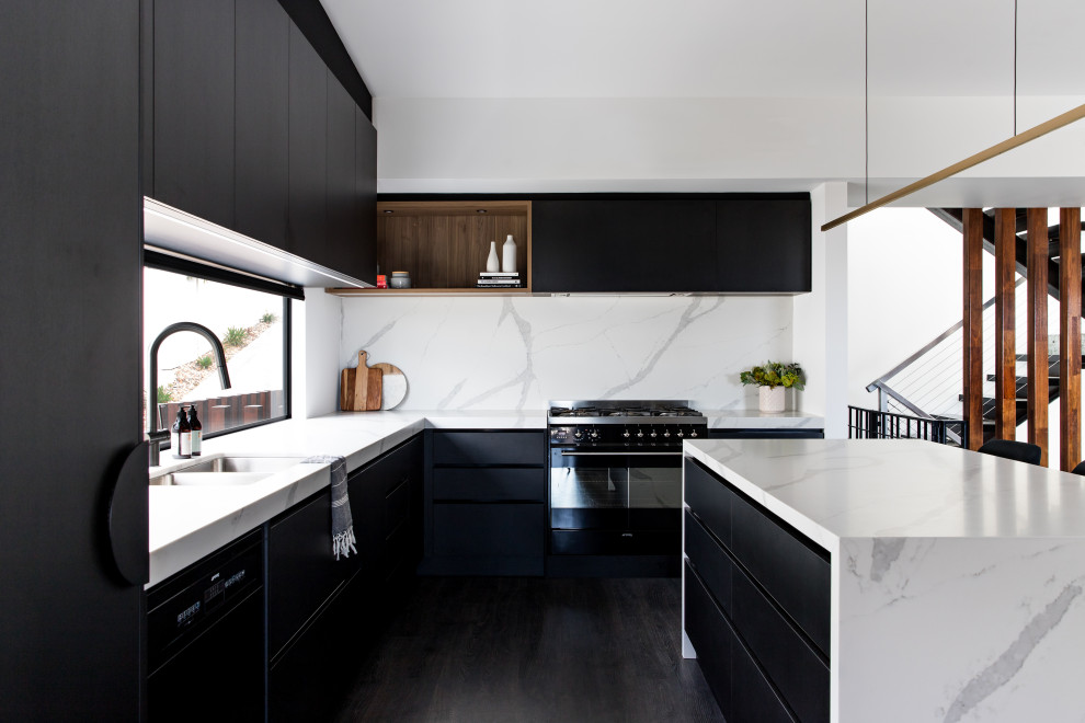 Стильный дизайн: угловая кухня в современном стиле с двойной мойкой, плоскими фасадами, белым фартуком, техникой под мебельный фасад, деревянным полом, островом, черным полом, белой столешницей и черно-белыми фасадами - последний тренд