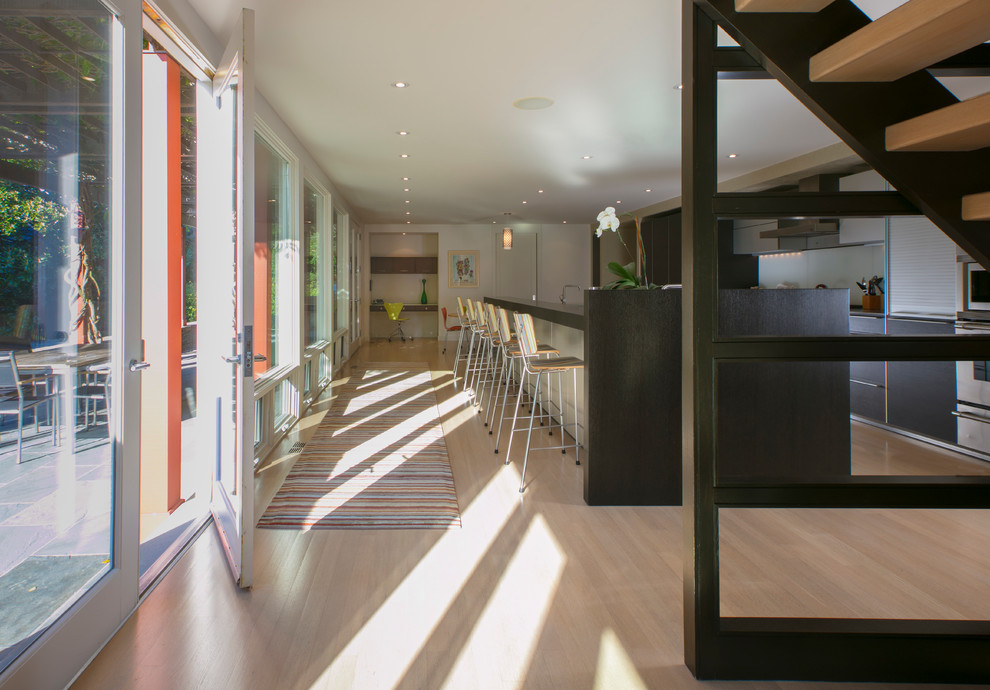 Immagine di un grande cucina con isola centrale design con ante lisce, ante in legno bruno, paraspruzzi con lastra di vetro, elettrodomestici in acciaio inossidabile e parquet chiaro