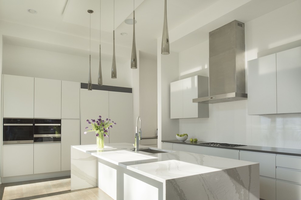 Design ideas for a medium sized modern galley enclosed kitchen in Atlanta with a built-in sink, flat-panel cabinets, white cabinets, marble worktops, white splashback, stainless steel appliances, light hardwood flooring and an island.