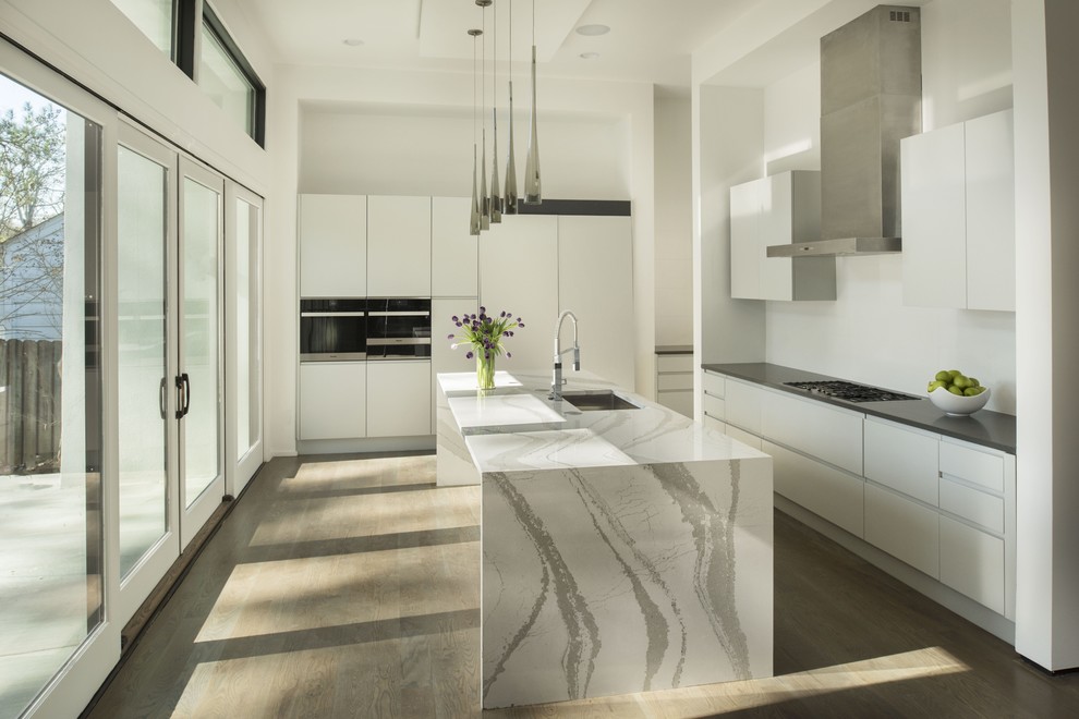 This is an example of a medium sized modern galley enclosed kitchen in Atlanta with a built-in sink, flat-panel cabinets, white cabinets, marble worktops, white splashback, stainless steel appliances, light hardwood flooring and an island.