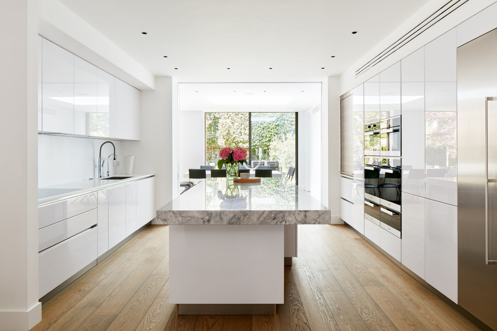 Modern inredning av ett stort kök, med en undermonterad diskho, släta luckor, vita skåp, marmorbänkskiva, vitt stänkskydd, mellanmörkt trägolv, en köksö, beiget golv och integrerade vitvaror