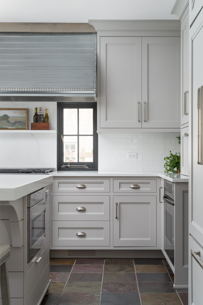 Inspiration for a medium sized farmhouse u-shaped kitchen/diner in Chicago with a belfast sink, flat-panel cabinets, grey cabinets, engineered stone countertops, white splashback, metro tiled splashback, integrated appliances, slate flooring, an island and white worktops.