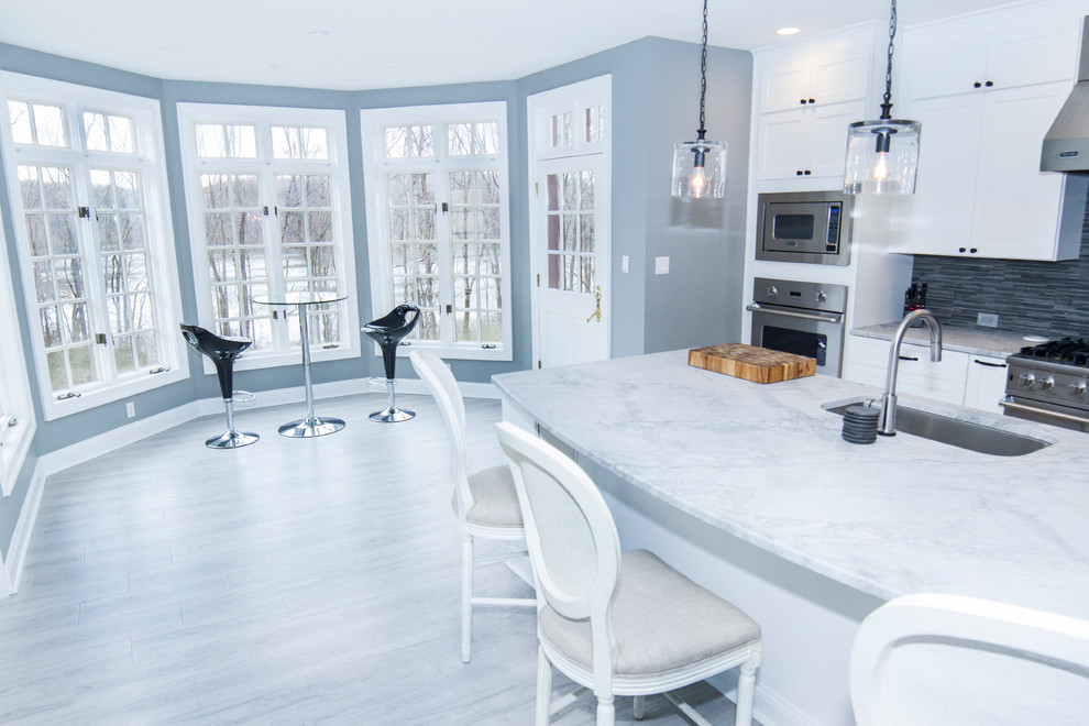 Bild på ett mellanstort funkis kök, med en undermonterad diskho, skåp i shakerstil, vita skåp, marmorbänkskiva, grått stänkskydd, stänkskydd i stickkakel, rostfria vitvaror, ljust trägolv, en köksö och grått golv