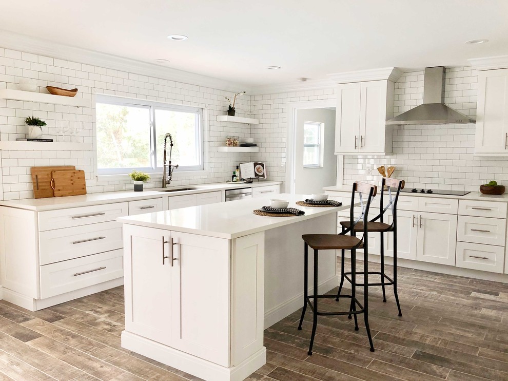 Design ideas for a classic kitchen in Orlando with a submerged sink, shaker cabinets, white cabinets, white splashback, metro tiled splashback, an island and brown floors.