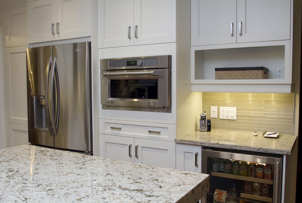 Modern inredning av ett stort kök, med en dubbel diskho, skåp i shakerstil, vita skåp, bänkskiva i kvarts, grått stänkskydd, stänkskydd i glaskakel, rostfria vitvaror, mellanmörkt trägolv och en köksö