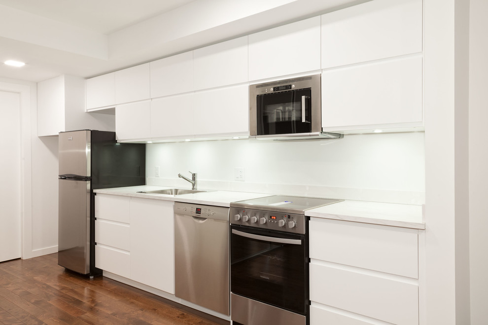 This is an example of a medium sized modern single-wall enclosed kitchen in Vancouver with a built-in sink, flat-panel cabinets, white cabinets, stainless steel appliances, medium hardwood flooring, brown floors, quartz worktops and no island.