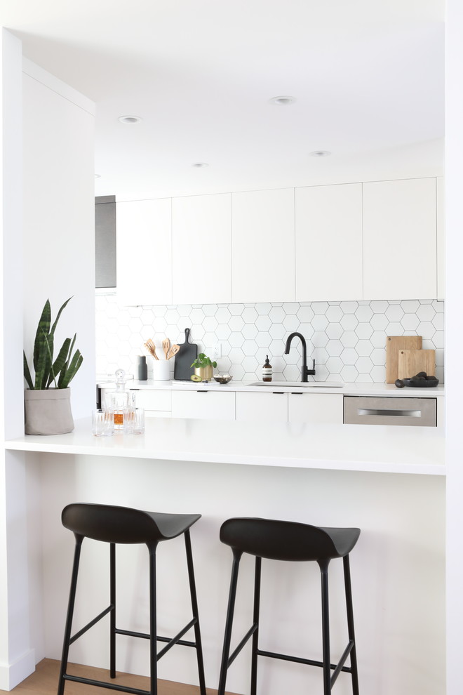Design ideas for a retro galley enclosed kitchen in Vancouver with a submerged sink, flat-panel cabinets, white cabinets, white splashback, cement tile splashback, stainless steel appliances, medium hardwood flooring, no island, brown floors and white worktops.