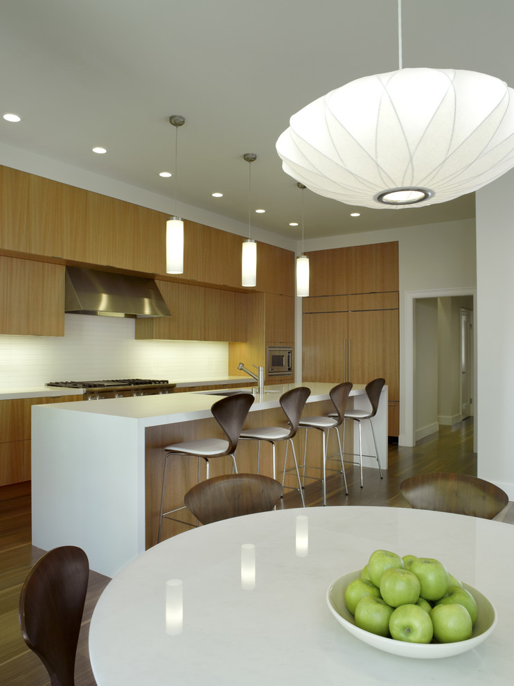 Идея дизайна: кухня в стиле модернизм с обеденным столом, плоскими фасадами, светлыми деревянными фасадами и техникой под мебельный фасад