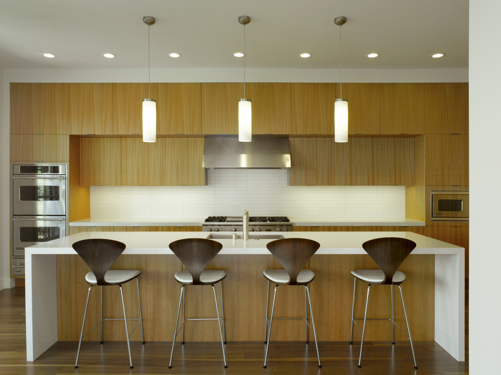 Immagine di una cucina parallela minimalista con elettrodomestici in acciaio inossidabile, lavello sottopiano, ante lisce, paraspruzzi bianco e ante in legno scuro