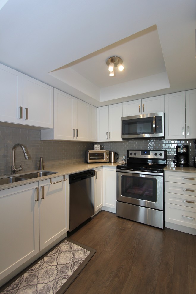 Open concept kitchen - small contemporary l-shaped dark wood floor and brown floor open concept kitchen idea in Toronto with an undermount sink, shaker cabinets, white cabinets, quartz countertops, gray backsplash, mosaic tile backsplash, stainless steel appliances and no island