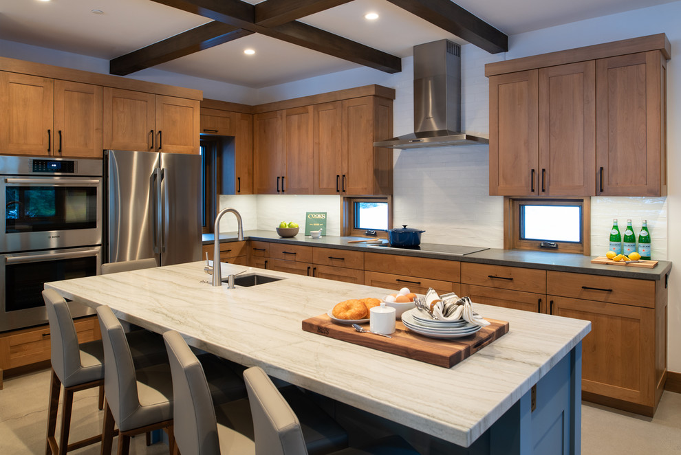 Mid-sized mountain style l-shaped concrete floor and gray floor kitchen photo in Other with a single-bowl sink, shaker cabinets, quartzite countertops, white backsplash, porcelain backsplash, stainless steel appliances, an island, white countertops and medium tone wood cabinets