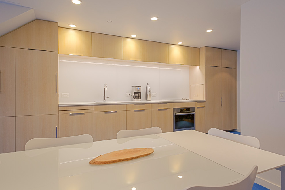 Foto på ett litet funkis linjärt kök och matrum, med en undermonterad diskho, släta luckor, skåp i ljust trä, bänkskiva i kvarts, vitt stänkskydd, glaspanel som stänkskydd, integrerade vitvaror, heltäckningsmatta och blått golv