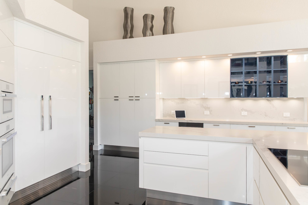 This is an example of an expansive modern l-shaped kitchen/diner in Miami with a submerged sink, flat-panel cabinets, white cabinets, engineered stone countertops, multi-coloured splashback, stone slab splashback, white appliances, marble flooring, an island, black floors and multicoloured worktops.