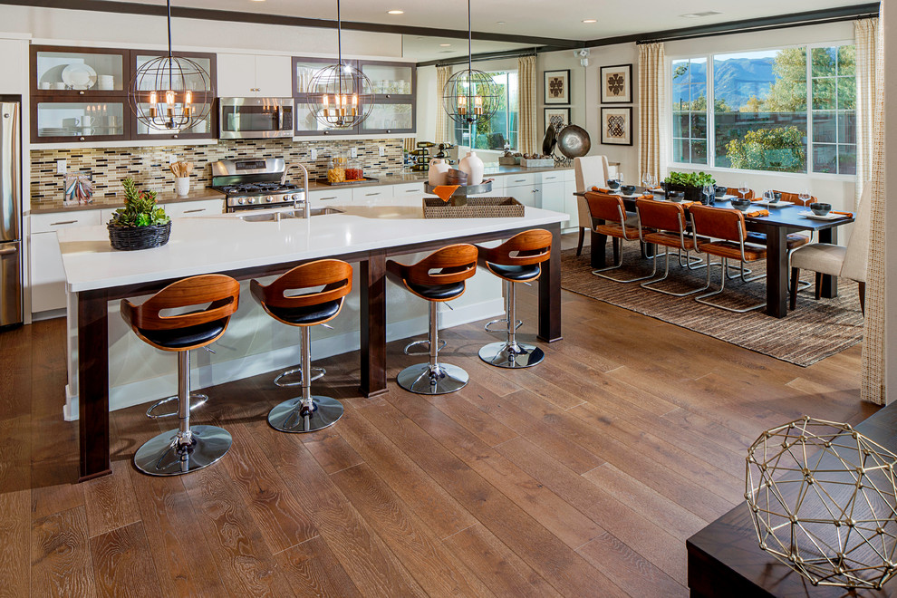 Large contemporary l-shaped kitchen/diner in Los Angeles with a submerged sink, flat-panel cabinets, white cabinets, engineered stone countertops, multi-coloured splashback, matchstick tiled splashback, stainless steel appliances, medium hardwood flooring, an island and brown floors.