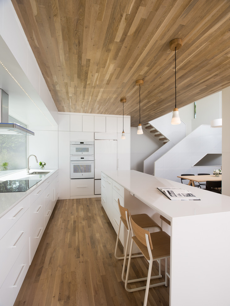 Example of a trendy l-shaped dark wood floor kitchen design in Minneapolis with an undermount sink, flat-panel cabinets, white cabinets, white appliances and an island