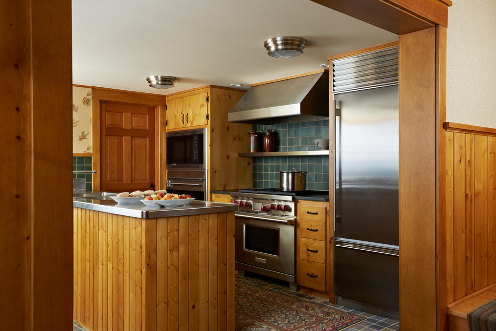 Mountain style galley enclosed kitchen photo in Minneapolis with an undermount sink, flat-panel cabinets, medium tone wood cabinets, stainless steel countertops, green backsplash, ceramic backsplash, stainless steel appliances and an island