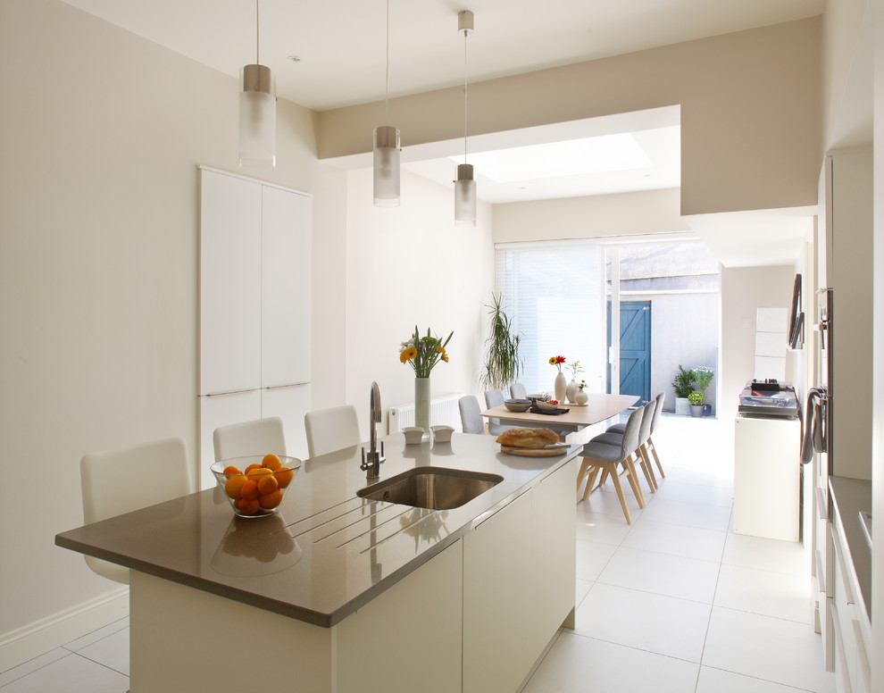 Diseño de cocina comedor moderna con armarios con paneles lisos, puertas de armario blancas, electrodomésticos de acero inoxidable y fregadero bajoencimera