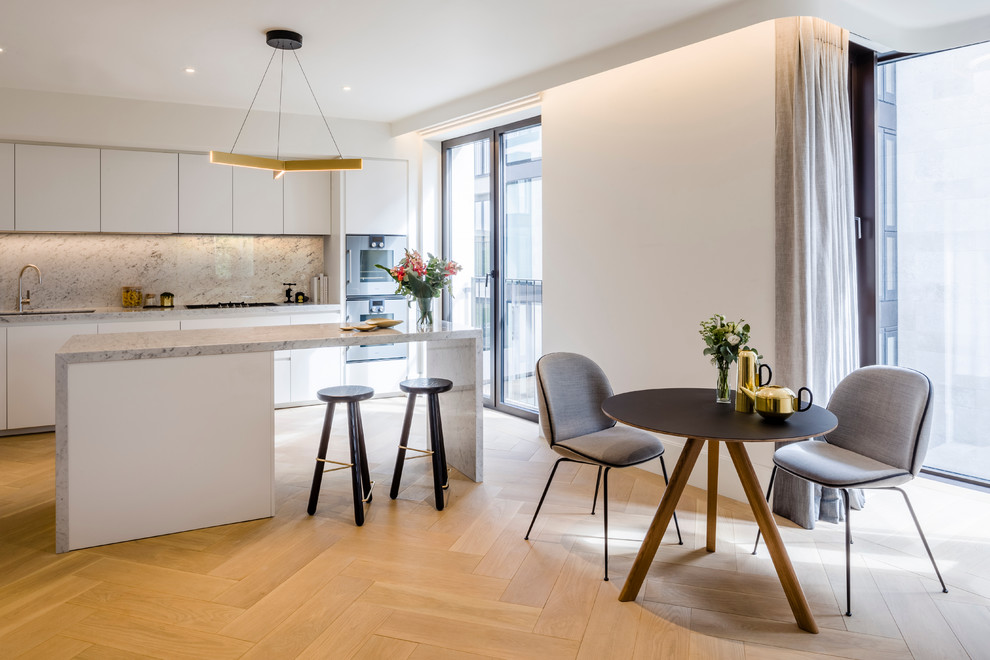 Zweizeilige Moderne Wohnküche mit flächenbündigen Schrankfronten, weißen Schränken, Küchenrückwand in Weiß, Rückwand aus Stein, braunem Holzboden und Kücheninsel in London