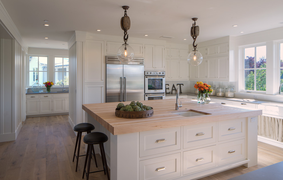 Kitchen - farmhouse l-shaped medium tone wood floor kitchen idea in San Francisco with a farmhouse sink, shaker cabinets, white cabinets, white backsplash, stainless steel appliances and an island
