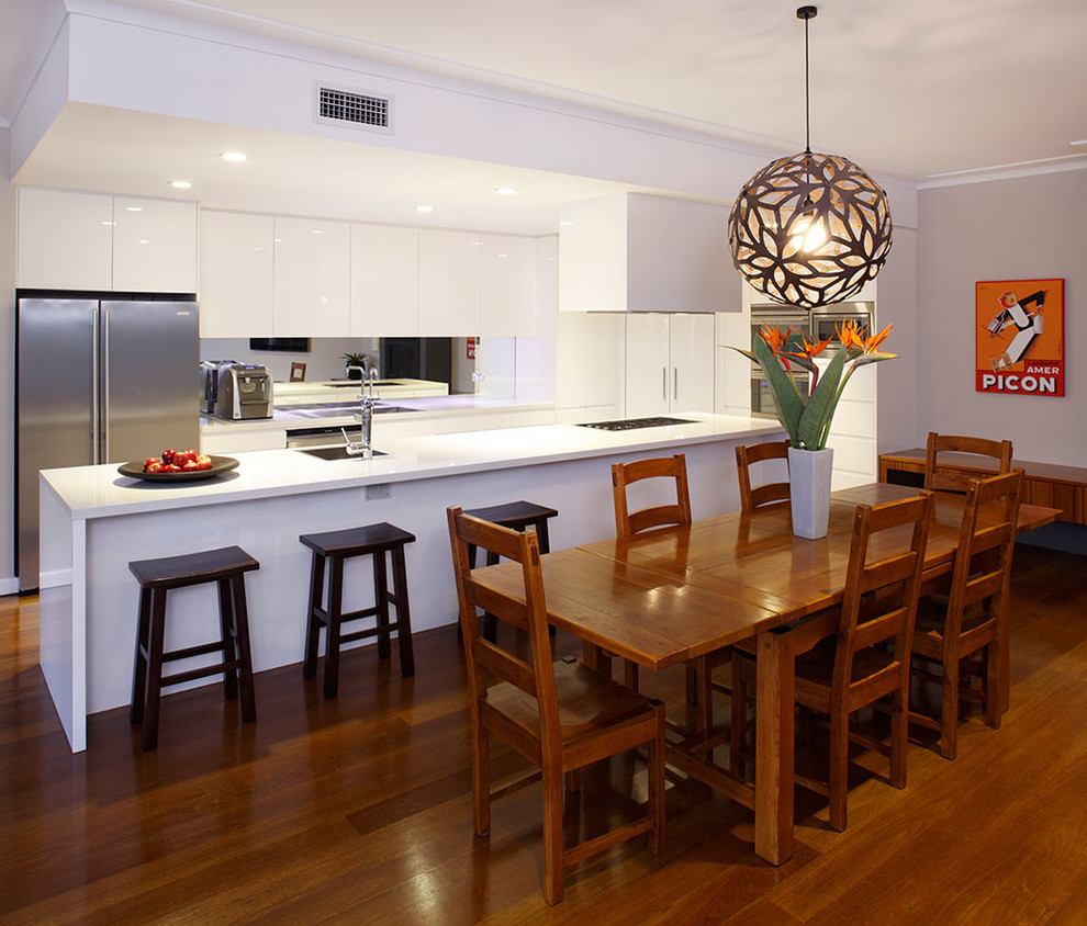Foto di una cucina moderna di medie dimensioni con ante lisce, ante bianche, top in granito, paraspruzzi a specchio, elettrodomestici in acciaio inossidabile e pavimento in legno massello medio