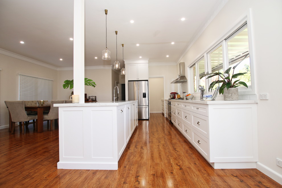 Exempel på ett stort klassiskt vit vitt kök, med en dubbel diskho, skåp i shakerstil, vita skåp, bänkskiva i kvarts, vitt stänkskydd, stänkskydd i tunnelbanekakel, rostfria vitvaror, mellanmörkt trägolv, en köksö och brunt golv