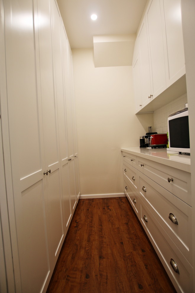 Bild på ett stort vintage vit vitt kök, med en dubbel diskho, skåp i shakerstil, vita skåp, bänkskiva i kvarts, vitt stänkskydd, stänkskydd i tunnelbanekakel, rostfria vitvaror, mellanmörkt trägolv, en köksö och brunt golv