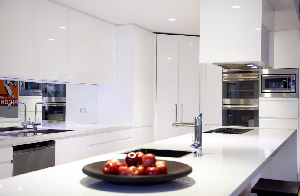 Idéer för ett mellanstort modernt kök, med en nedsänkt diskho, släta luckor, vita skåp, bänkskiva i glas, spegel som stänkskydd, mellanmörkt trägolv, en köksö, stänkskydd med metallisk yta och rostfria vitvaror