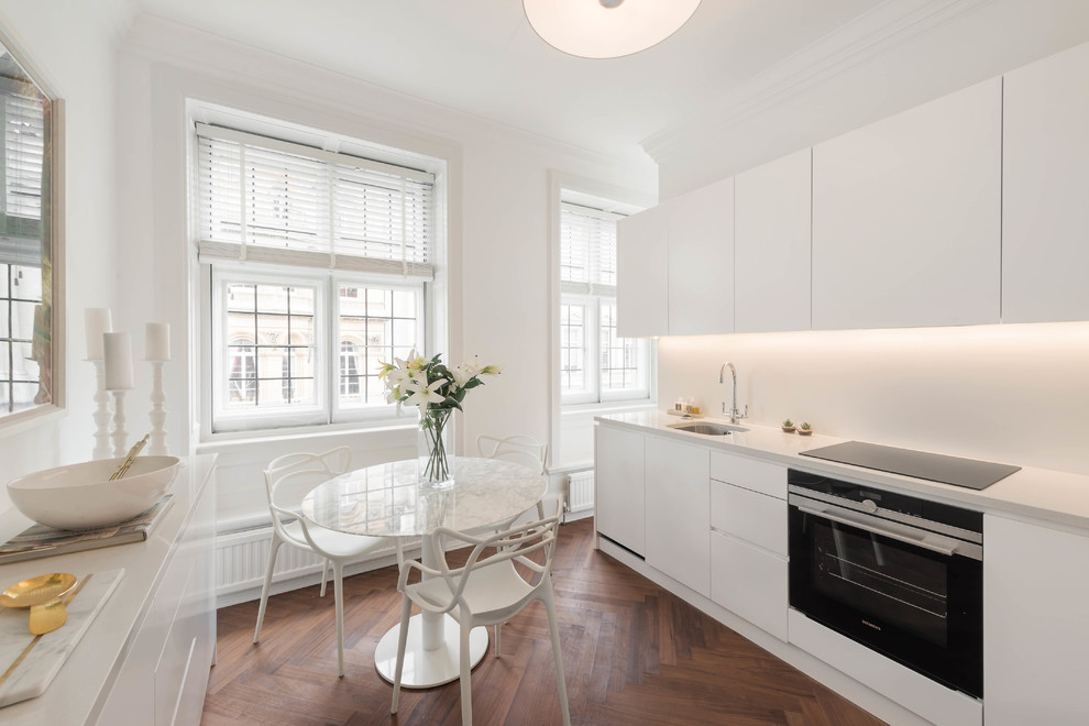 Zweizeilige, Kleine Moderne Wohnküche mit Unterbauwaschbecken, flächenbündigen Schrankfronten, weißen Schränken, dunklem Holzboden und braunem Boden in London